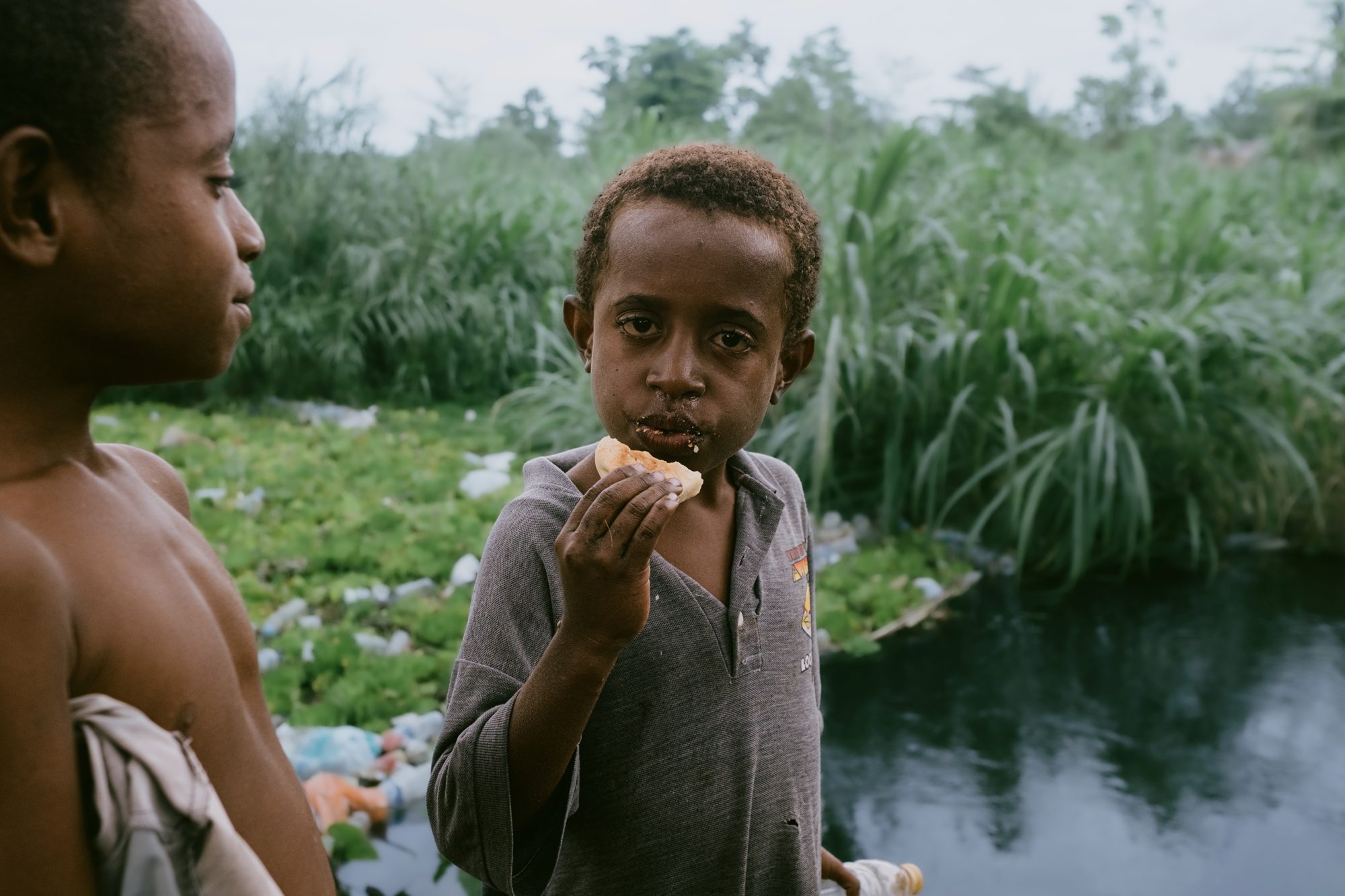 Two boys by the river greet a passing stranger